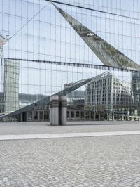 a building is reflected in the mirrored windows of a glass wall and stone pavement outside