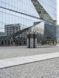 a building is reflected in the mirrored windows of a glass wall and stone pavement outside