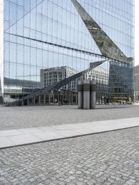 a building is reflected in the mirrored windows of a glass wall and stone pavement outside