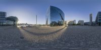 a very large glass building reflecting another large glass building in it's reflection on some cobblestone