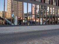 reflection of the glass building in the windows on the street outside, a bench outside, and other buildings