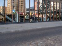 reflection of the glass building in the windows on the street outside, a bench outside, and other buildings