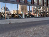 reflection of the glass building in the windows on the street outside, a bench outside, and other buildings