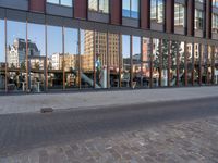 reflection of the glass building in the windows on the street outside, a bench outside, and other buildings