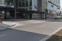 an empty street with a few people walking and standing near some glass building and a street light