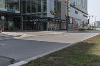 an empty street with a few people walking and standing near some glass building and a street light