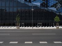 a empty street next to a tall black glass building with trees and concrete benches on the sidewalk