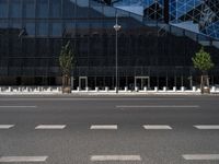 a empty street next to a tall black glass building with trees and concrete benches on the sidewalk