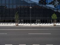 a empty street next to a tall black glass building with trees and concrete benches on the sidewalk