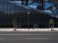 a empty street next to a tall black glass building with trees and concrete benches on the sidewalk