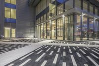 an empty city sidewalk next to a building with glass doors and windows in the evening