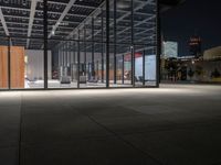 a building with a lot of windows and concrete flooring, at night time, in front of it