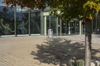 a sidewalk with trash cans next to an office building and trees on the outside side