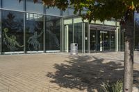 a sidewalk with trash cans next to an office building and trees on the outside side