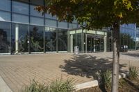 a sidewalk with trash cans next to an office building and trees on the outside side