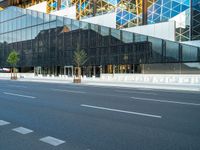 an empty road passing under a modern glass structure that is reflecting the sunset and the sky