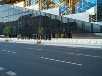 an empty road passing under a modern glass structure that is reflecting the sunset and the sky