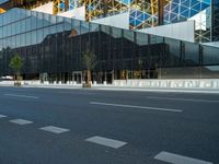 an empty road passing under a modern glass structure that is reflecting the sunset and the sky