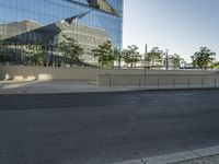 this empty parking lot is located at the corner of a modern, glass building with reflections on the sides