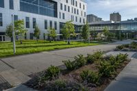 a city street surrounded by grass and tall buildings at the end of a street there is a paved pathway in front of the building