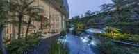 a pond and garden is outside the glass house by the water fall of tropical trees