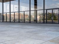 the empty sidewalk is next to some large windows with glass walls on them, reflecting the surrounding buildings