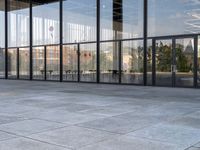 the empty sidewalk is next to some large windows with glass walls on them, reflecting the surrounding buildings