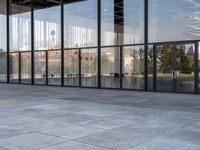 the empty sidewalk is next to some large windows with glass walls on them, reflecting the surrounding buildings