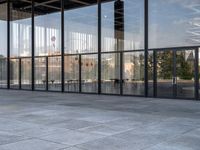 the empty sidewalk is next to some large windows with glass walls on them, reflecting the surrounding buildings