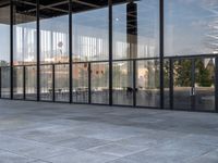 the empty sidewalk is next to some large windows with glass walls on them, reflecting the surrounding buildings