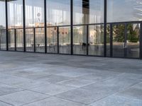 the empty sidewalk is next to some large windows with glass walls on them, reflecting the surrounding buildings