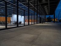 the inside of a building that has glass walls and benches outside it at night in an urban area