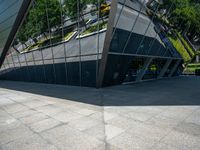 a large silver building with many windows and mirrors on it's face near a sidewalk