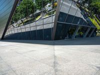 a large silver building with many windows and mirrors on it's face near a sidewalk