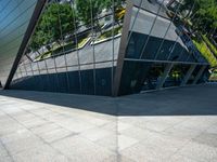 a large silver building with many windows and mirrors on it's face near a sidewalk