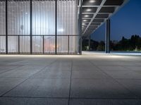 a empty building with an open glass wall and lighting in it at night time with people walking outside