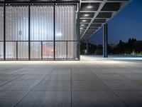 a empty building with an open glass wall and lighting in it at night time with people walking outside