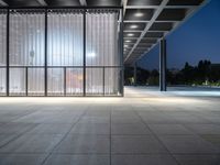 a empty building with an open glass wall and lighting in it at night time with people walking outside