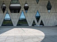 the shadow of the person is on the ground by a building with triangular windows on the side