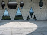 the shadow of the person is on the ground by a building with triangular windows on the side