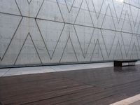 a wooden bench sits against a concrete wall that has geometric designs on it while others sit in the background