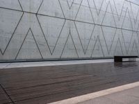 a wooden bench sits against a concrete wall that has geometric designs on it while others sit in the background