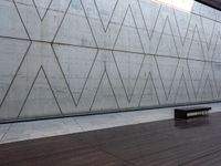 a wooden bench sits against a concrete wall that has geometric designs on it while others sit in the background