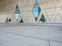 a person walking in front of an office building with windows and triangular designs on the facade