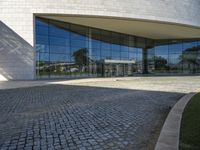 a modern building is featured behind a glass wall at the entrance of the building, which sits on a stone pathway