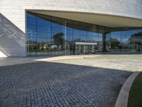 a modern building is featured behind a glass wall at the entrance of the building, which sits on a stone pathway