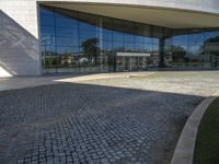 a modern building is featured behind a glass wall at the entrance of the building, which sits on a stone pathway