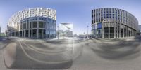 a wide angle photo of two large glass - walled buildings across an empty road from each other