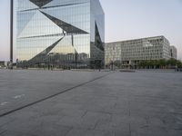 two buildings with a glass wall in an empty plaza in the city center of london