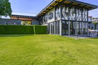 the glass walled patio and garden area has outdoor furniture on top of it with green hedges